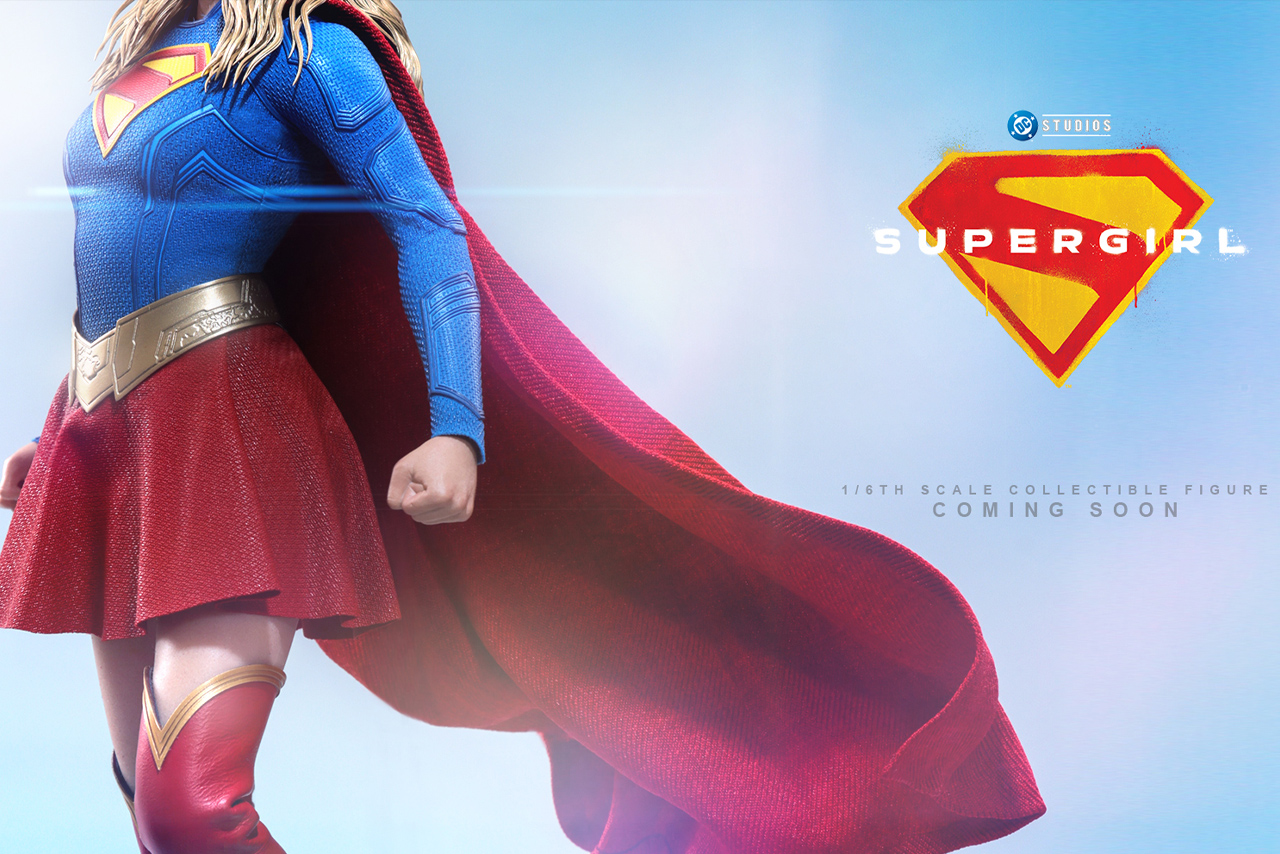 Side profile teaser image of the Hot Toys Supergirl 1/6 Scale Figure showcasing a blue textured suit, red cape, gold belt, red skirt, and the DC Studios Supergirl movie logo.